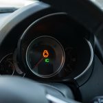 Gros plan réaliste du tableau de bord d’une voiture avec le voyant moteur allumé, reflets discrets sur les compteurs et éclairage naturel, style photo de presse automobile.