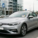Voiture récente vue de trois quarts avant, avec une vignette écologique colorée visible sur le pare-brise, à l’entrée d’une zone urbaine à faibles émissions.