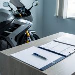 Carte grise moto sans certificat de cession : peut-on l’obtenir ? Moto moderne placée près d’un bureau avec un dossier administratif vierge et des formulaires non remplis, évoquant une démarche d’immatriculation.